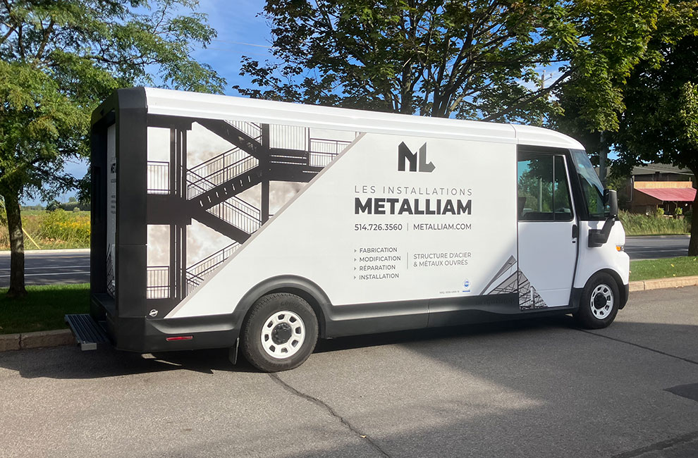 Vue du côté du véhicule de service blanc de Les installations Metalliam avec un wrap partiel avec des photos noir et blanc de structures en acier et une liste des services offerts en-dessous du logo.