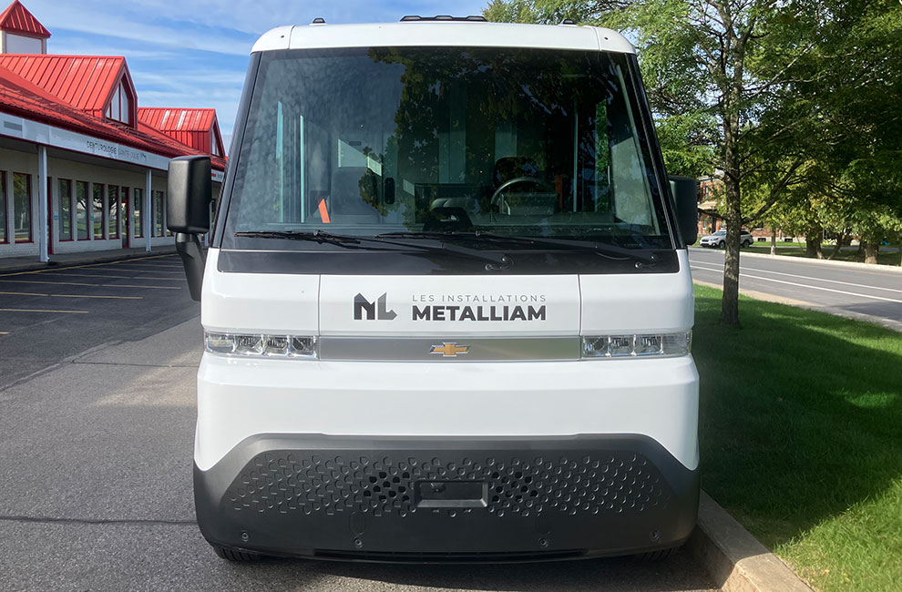 Vue de l'avant du véhicule de service blanc de Les installations Metalliam avec le logo installé en-dessous du pare-prise