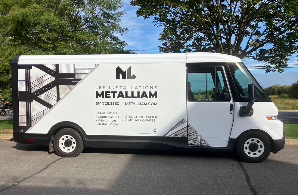 Vue de côté du véhicule de service blanc de Les installations Metalliam avec un wrap partiel avec des photos noir et blanc de structures en acier et une liste des services offerts en-dessous du logo.