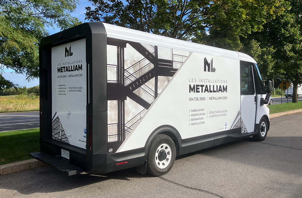 Vue de l'arrière du véhicule de service blanc de Les installations Metalliam avec un wrap partiel avec des photos noir et blanc de structures en acier et une listes des services offerts en-dessous du logo.